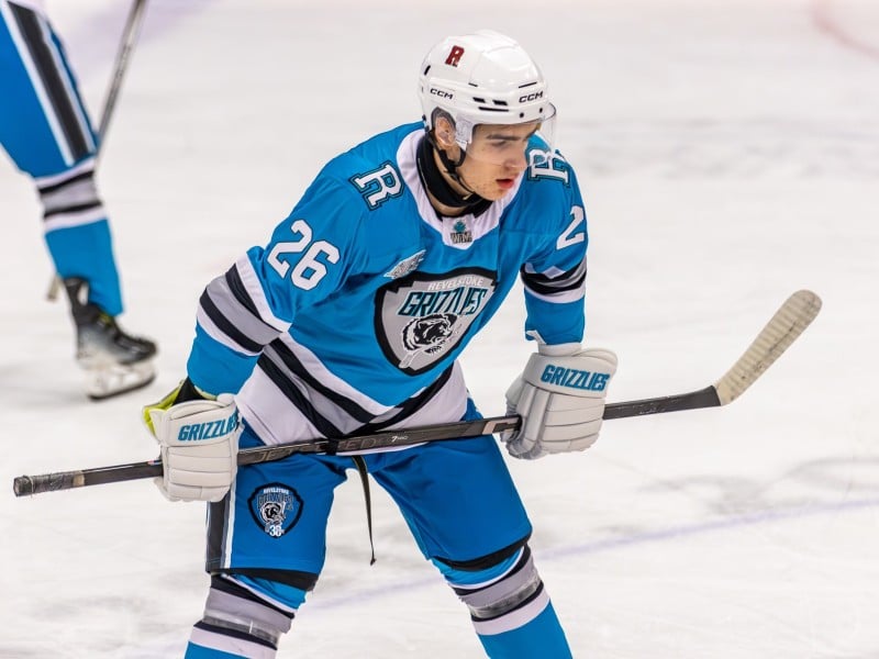 Connor Shymoniak, Revelstoke Grizzlies player in the blue Revelstoke Grizzlies jersey. He is on the ice, staring towards the other end, hands on knees and stick braced.