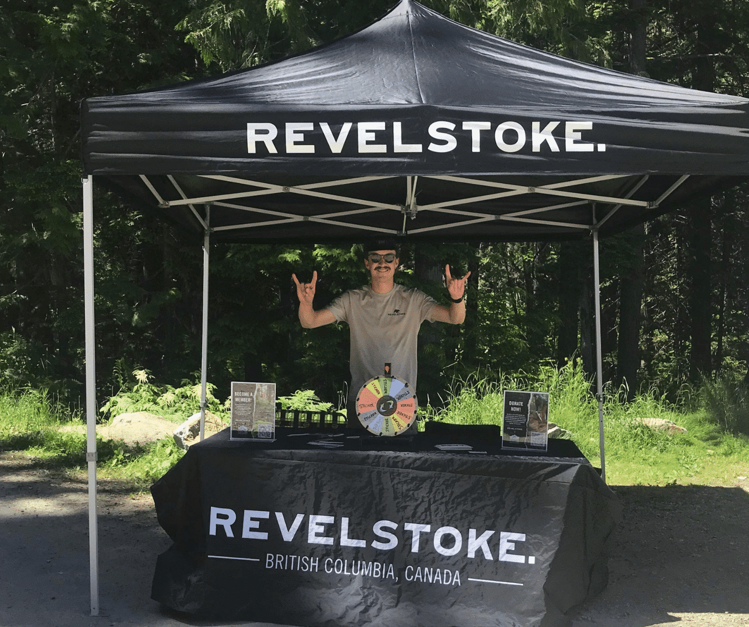 Tourism Revelstoke Stoke Team member standing behind a Tourism Revelstoke branded table, holding up Downtown Dollars