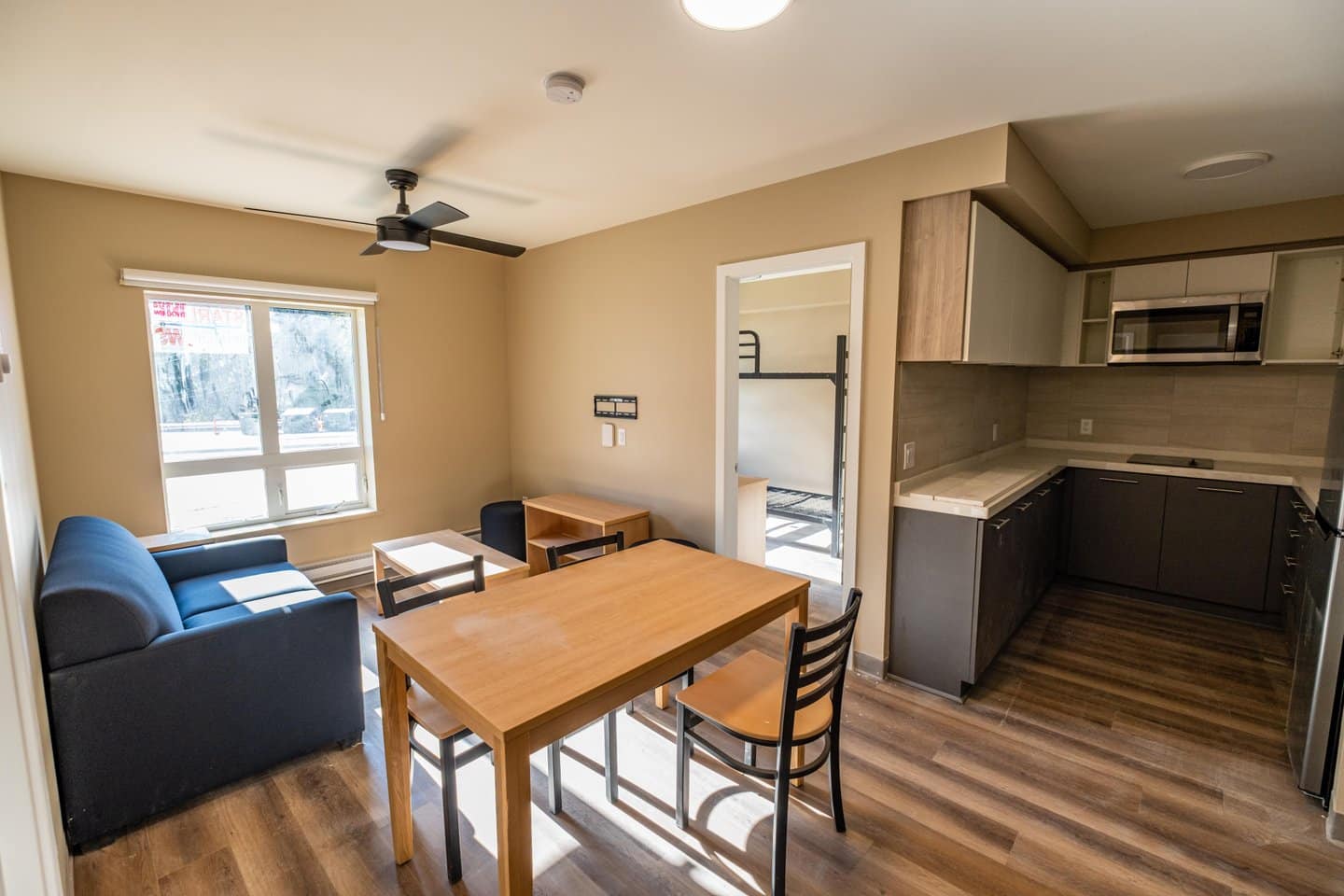 Interior of a Revelstoke Mountain Resort staff housing unit, showing a couch, table, kitchen and a bedroom with bunk beds.