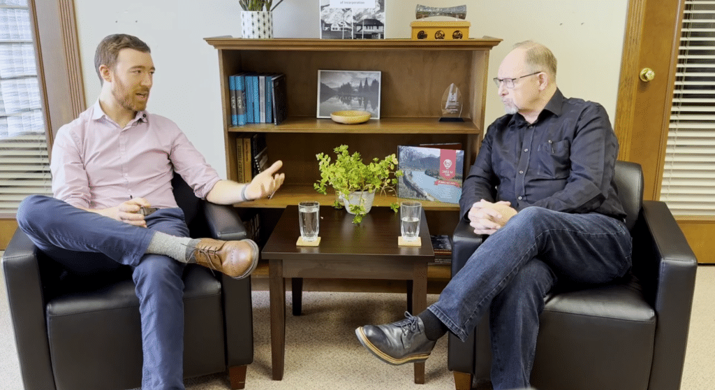 Paul Simon, a younger white man and Gary Sulz, and older white man sitting in chairs partially facing each other in an office and talking about Revelstoke STRs