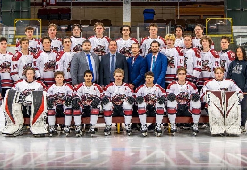 Revelstoke Grizzlies team photo on the ice of the Revelstoke Forum. The players are dressed in their gear, support and coach staff wearing suits.