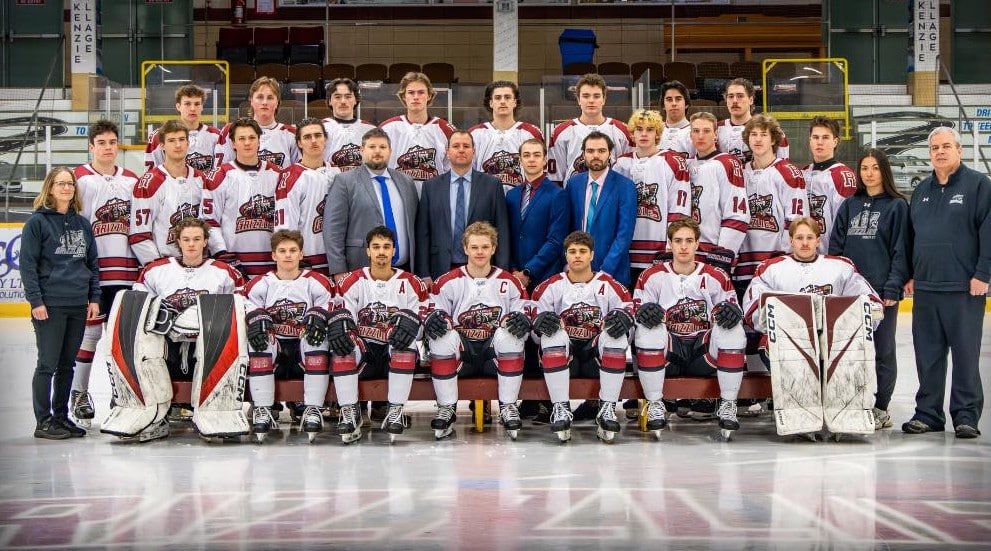 Revelstoke Grizzlies team photo on the ice of the Revelstoke Forum. The players are dressed in their gear, support and coach staff wearing suits.