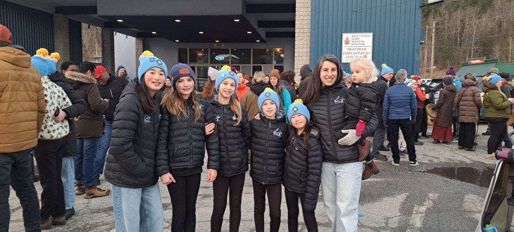 Youth Revelstoke Skating Club teammates in their black jackets, standing in a line in front of the Revelstoke Legion at the coffee break during the Coldest Night of the Year walk