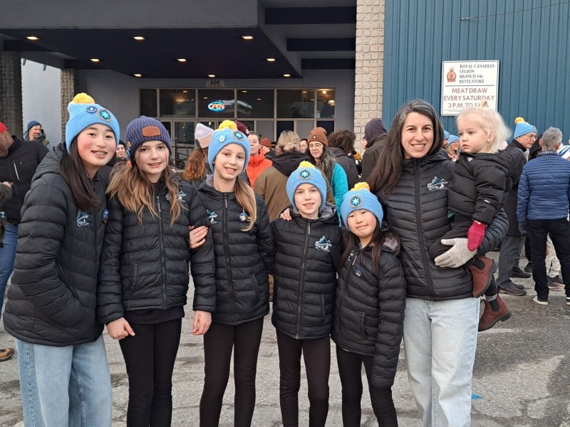 Youth Revelstoke Skating Club teammates in their black jackets, standing in a line in front of the Revelstoke Legion at the coffee break during the Coldest Night of the Year walk