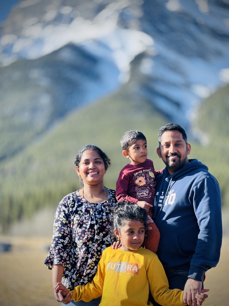 Southern Curry House owners Kokila Marikannan and Marikannan Thangaraj and their two children in a family portrait in front of a mountain scene.