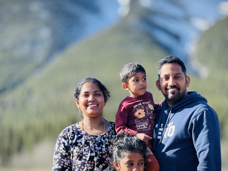 Southern Curry House owners Kokila Marikannan and Marikannan Thangaraj and their two children in a family portrait in front of a mountain scene.