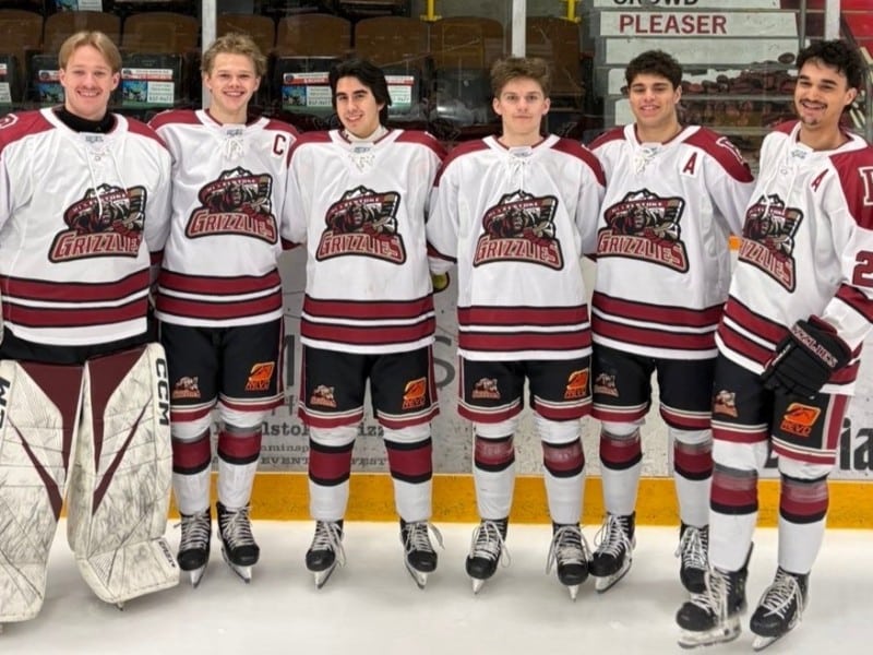 Six Revelstoke Grizzlies players in their gear, standing in a line with arms over each other's shoulders as they all look at the camera and smile.