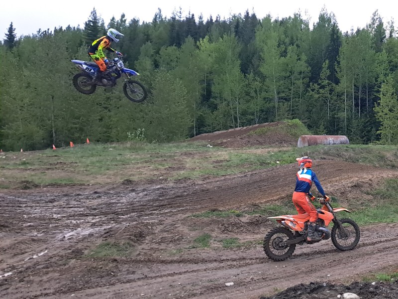 A Future West Moto Cross dirtbike racer taking a jump while another racer looks back at them in the air. Both are on the Revy Riders Dirtbike Club race course