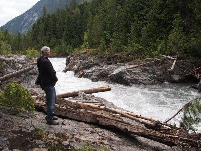 Steve Black stands on a rock cliff overlooking a very high Illecillewaet River now clear of the Box Canyon log jam. There are bits of logs on either side of the river still.
