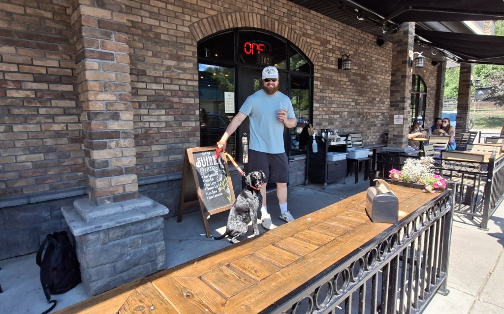 A dog and owner stand in front of the La Baugette door leading to the Revelstoke dog-friendly patio.