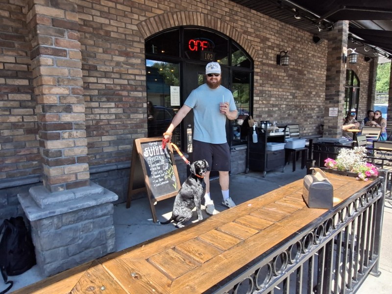 A dog and owner stand in front of the La Baugette door leading to the Revelstoke dog-friendly patio.