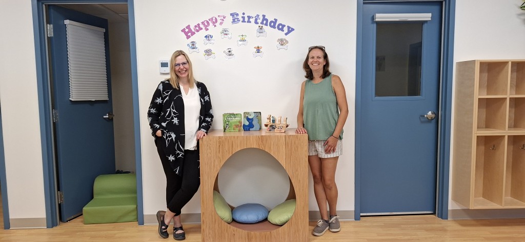 Two women standing on either side of a comfort cube sitting spot in the new Revelstoke Child Care Society classroom