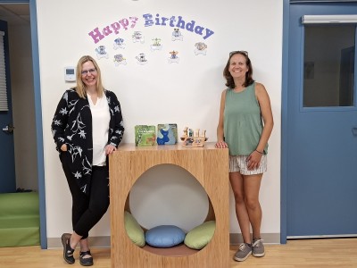 Two women standing on either side of a comfort cube sitting spot in the new Revelstoke Child Care Society classroom